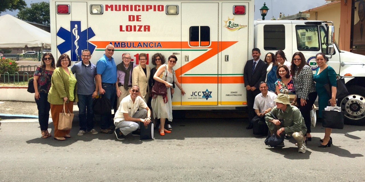 Photo of participants from AJC’s Fact-Finding and Solidarity Mission to Puerto Rico, organized in the aftermath of Hurricane Maria in May 2018, pose in front of an ambulance in the coastal town of Loiza.