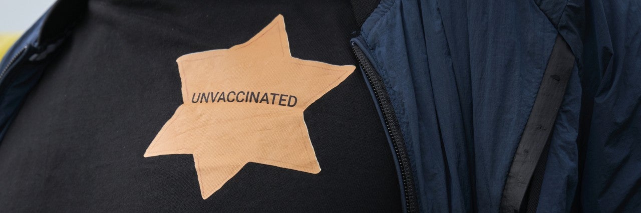 Anti-vax protestor wearing star of David unvaccinated sign