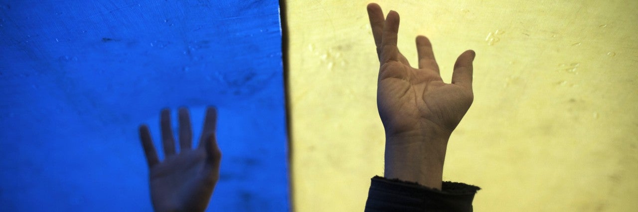 image of two raised hands and wrists in front of a ukranian flag, half yellow, half blue