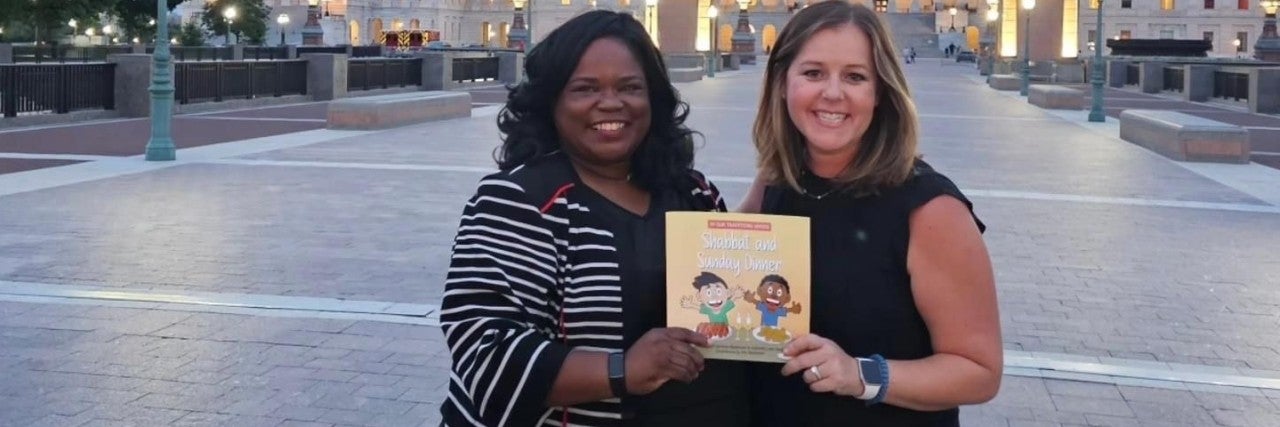 Left - Candace Bazemore. Right - Gabby Leon Spatt, holding the book "Shabbat and Sunday Dinner". Both are smiling in front of the Capitol building in Washington, DC.