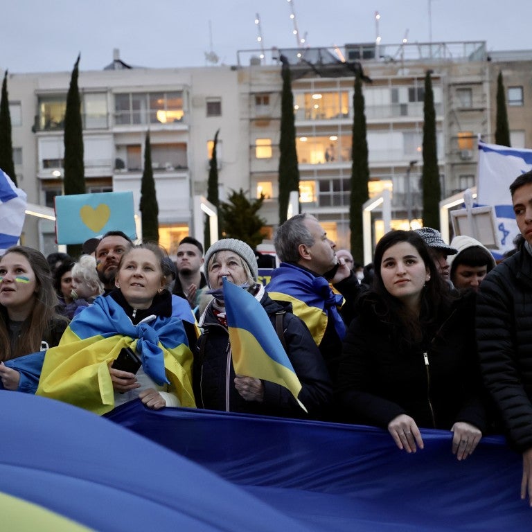 Israelis holding banners and flags while watching Ukrainian President Volodymyr Zelensky's speech at the Knesset in Israel