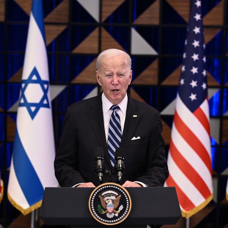 President Joe Biden standing in front a lectern, flanked by four flags: US flag, israel flag, followed by US flag and Israel flag