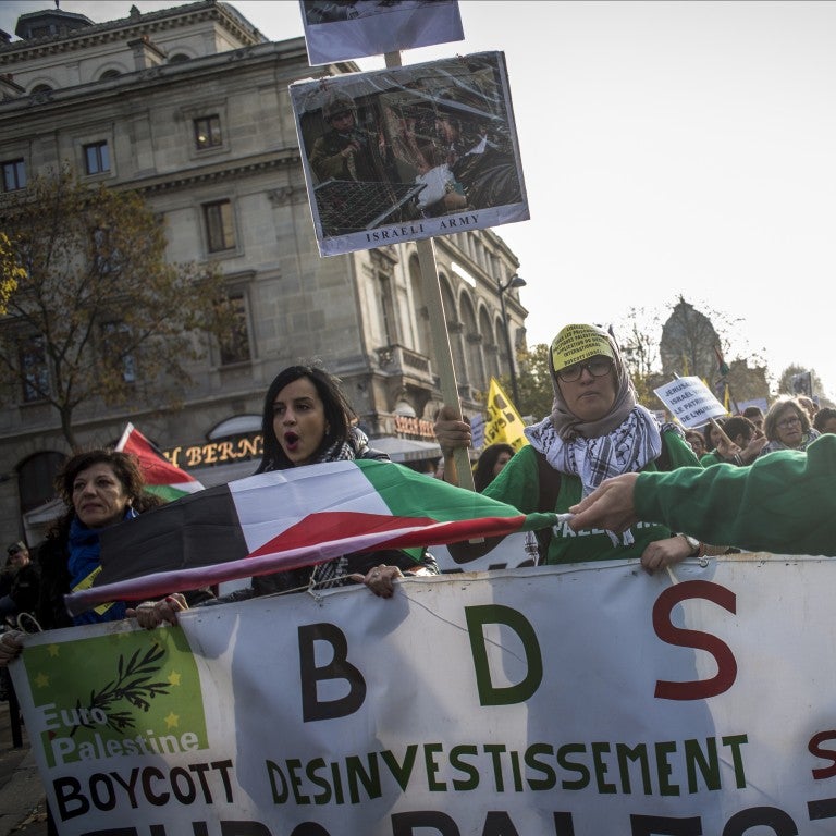 image of people in france marching holding a sign that reads BDS and french writing