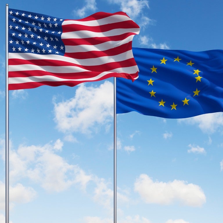 Photo of an American flag and a European Union flag waving side-by-side