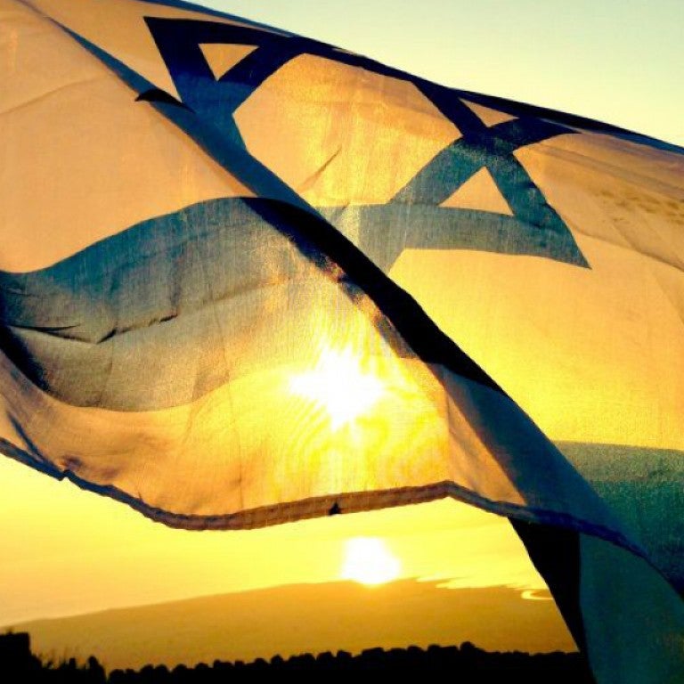 Photo of Israeli flag waving with a sunset in the background